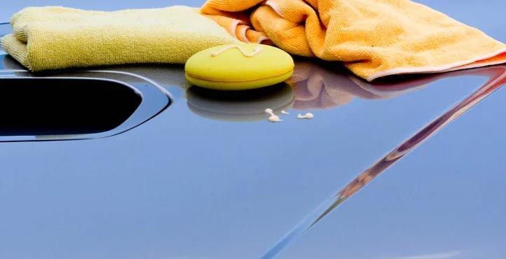 Yellow cloths and sponge cleaning a blue car hood near the windshield opening