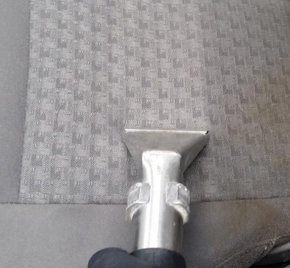 Close-up of a metal vacuum cleaner nozzle on gray patterned upholstery