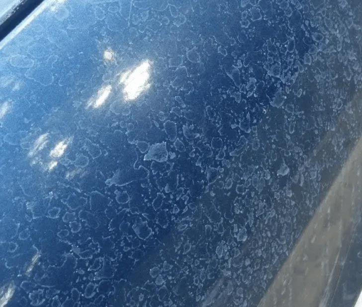 Close-up of a blue car hood with water spots and bright reflections