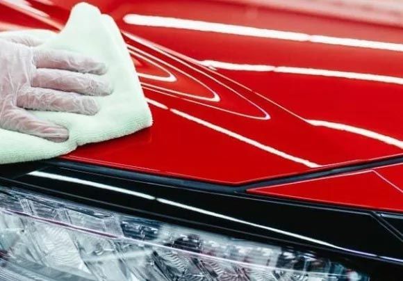 Gloved hand polishing a red car hood above the headlight