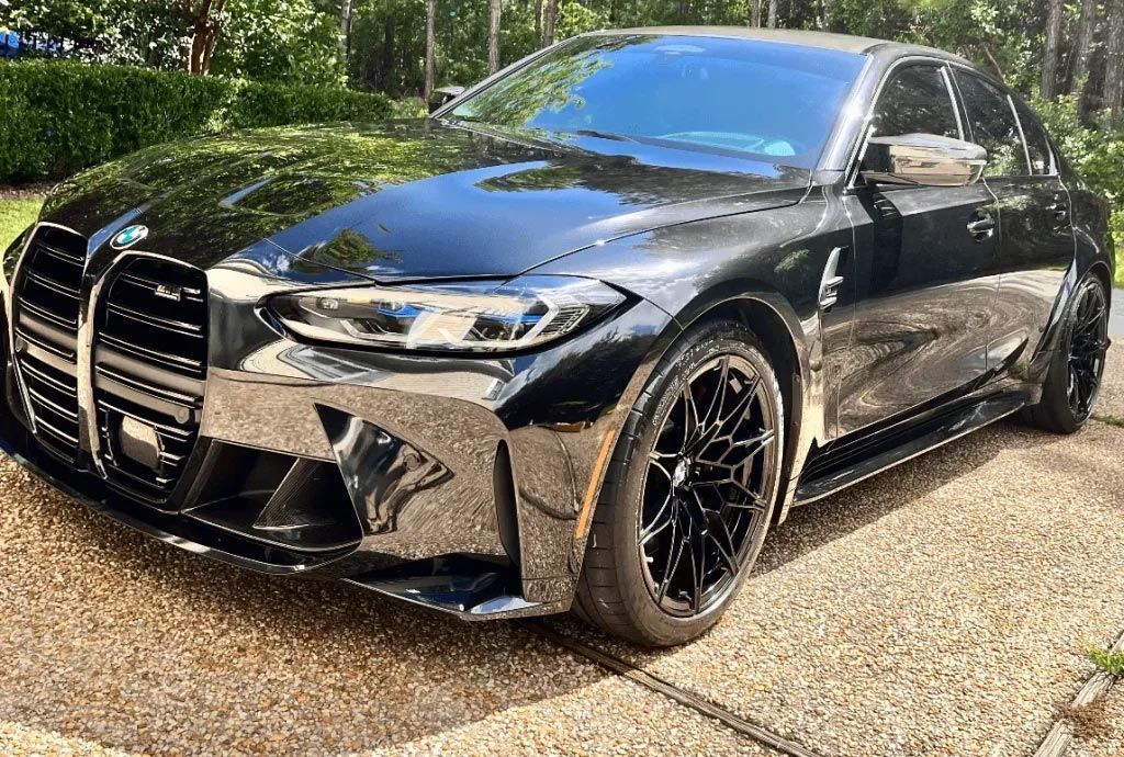 Black BMW sedan parked on a gravel driveway in a sunny wooded area