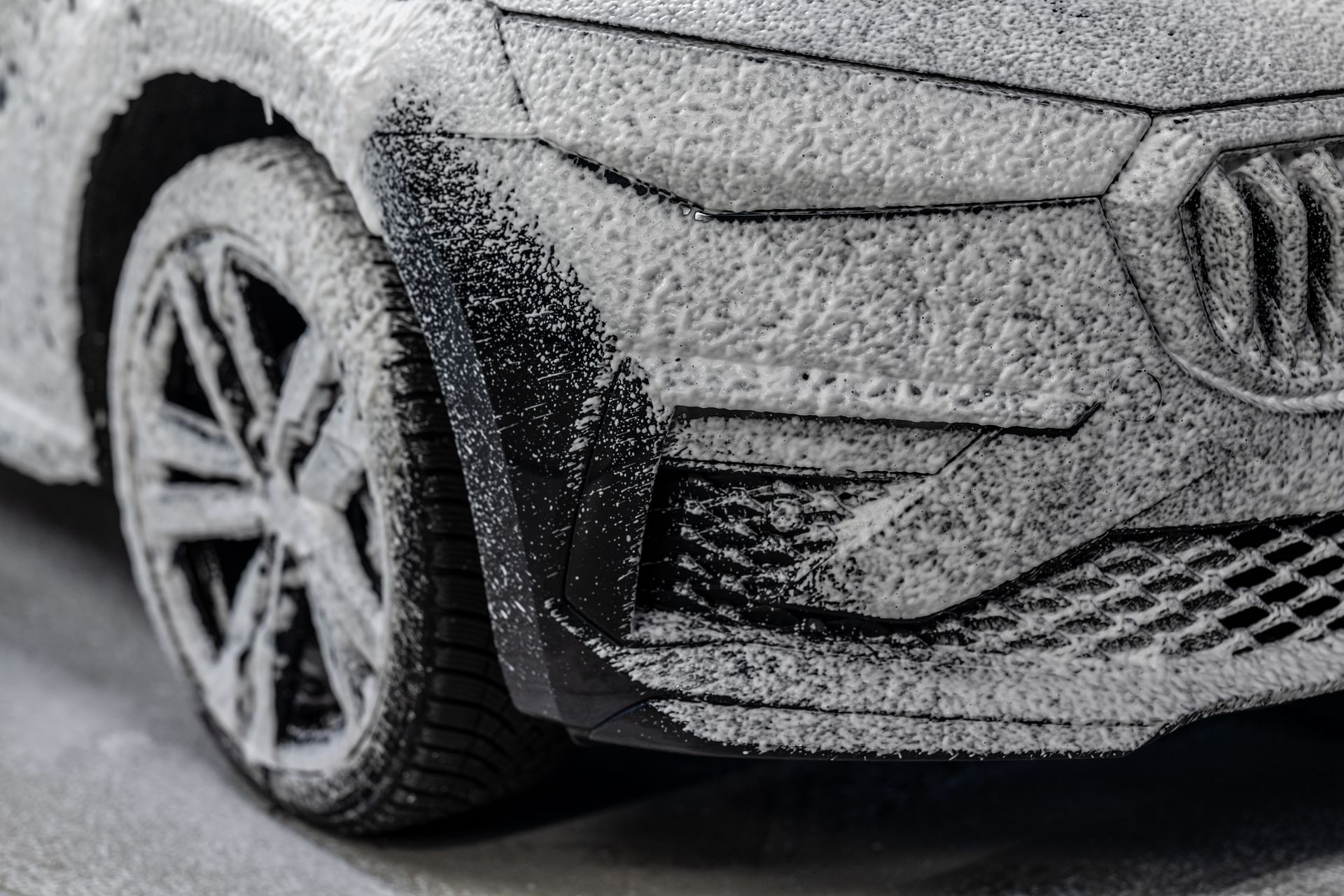 Close-up of a snow-covered car wheel and front bumper in winter conditions
