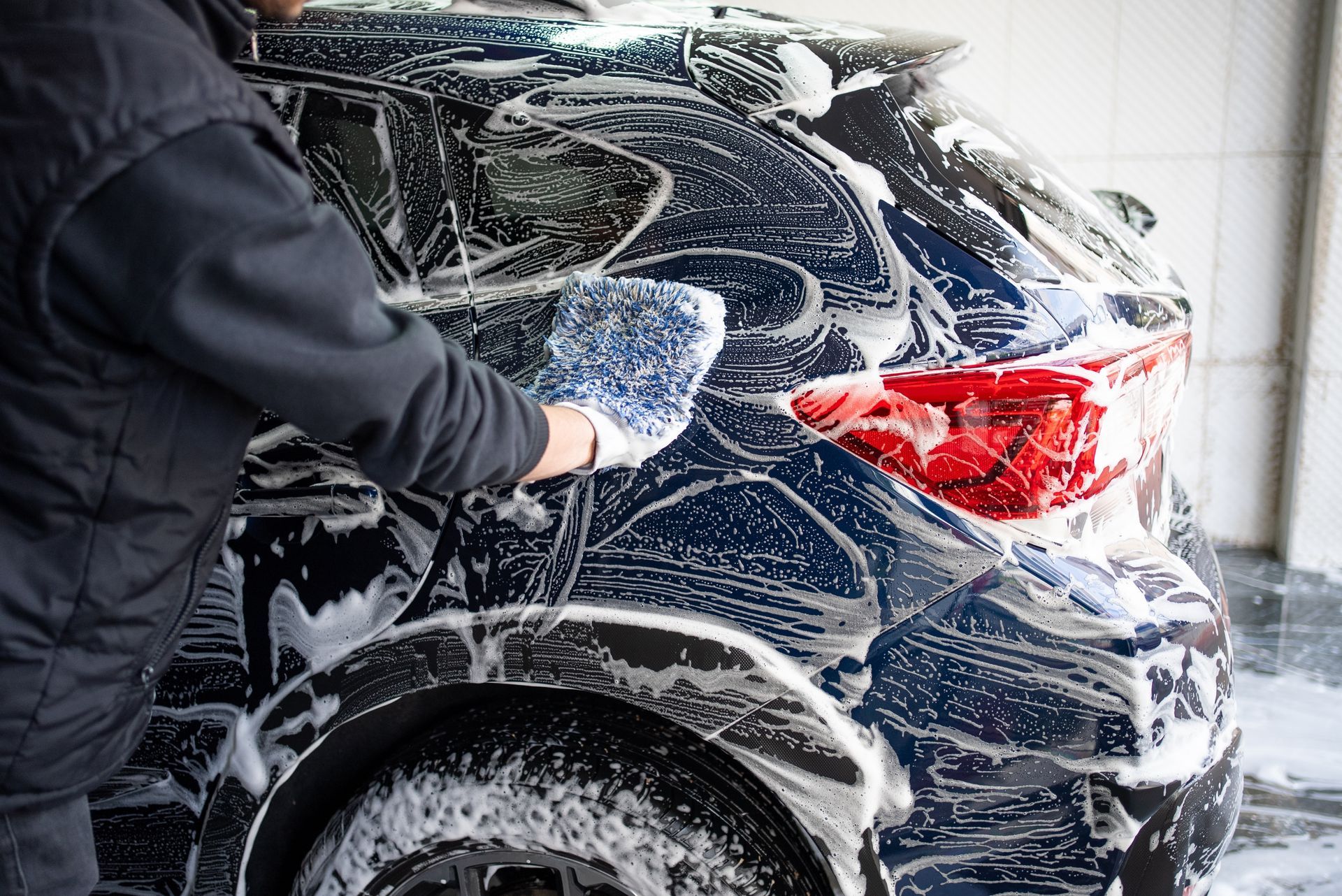Person washing a dark blue SUV with soap foam at a car wash
