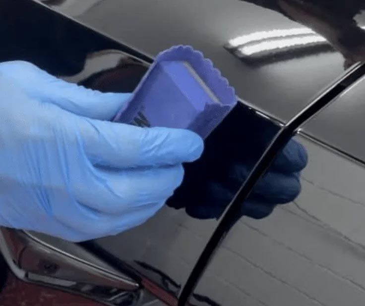 Blue-gloved hand applying a purple applicator to a black car panel