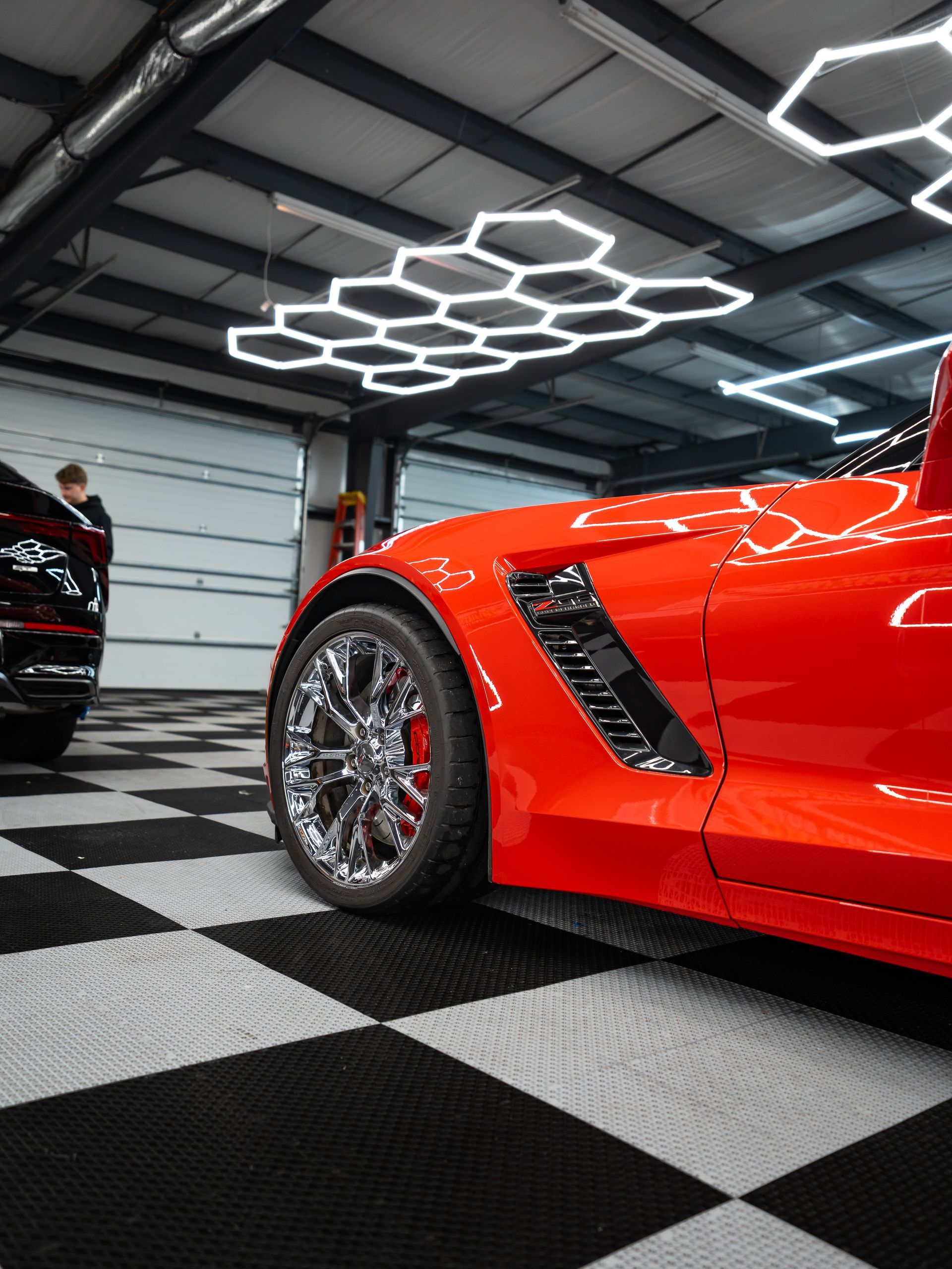 Red sports car in a modern garage with black-and-white checkered floor and hexagonal ceiling lights