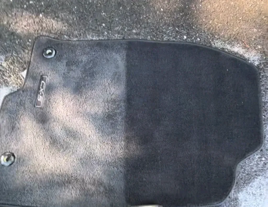 Black car floor mat with two metal eyelets on a gray surface