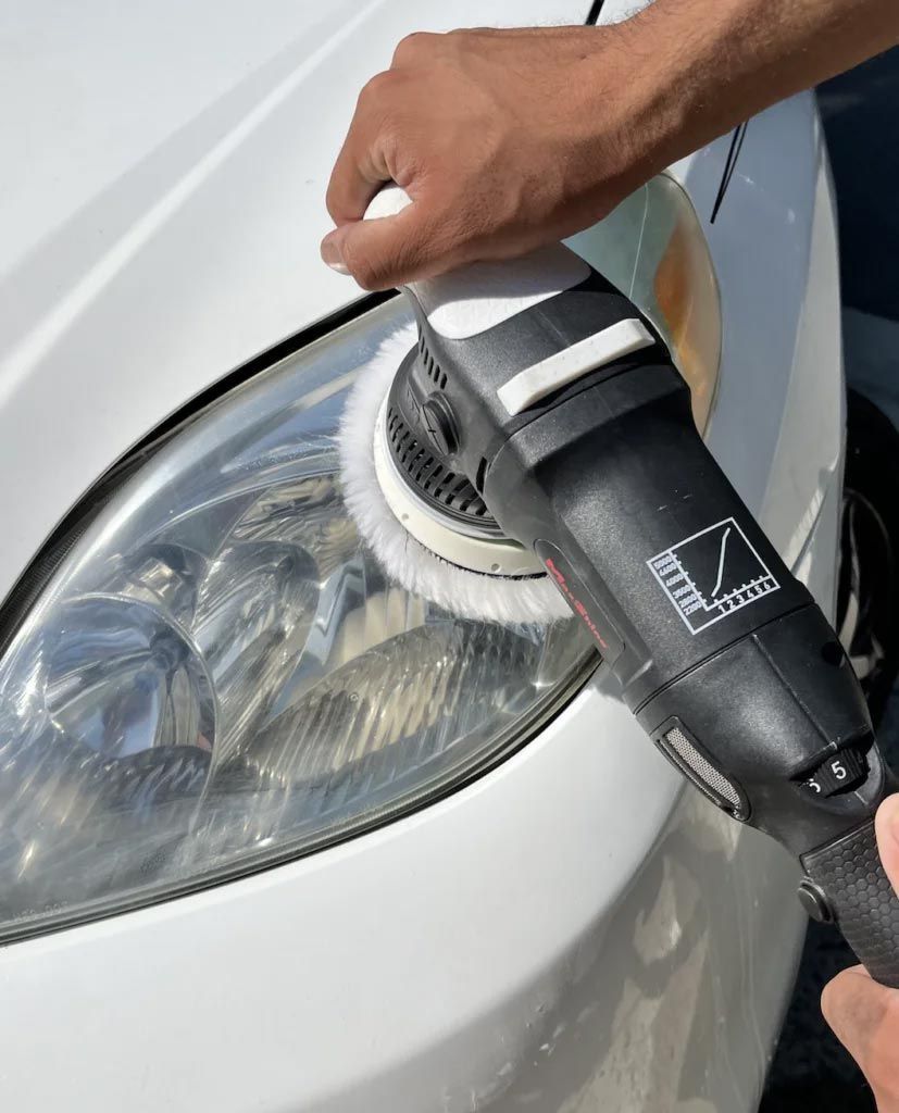 Person polishing a white car headlight with a black buffer tool