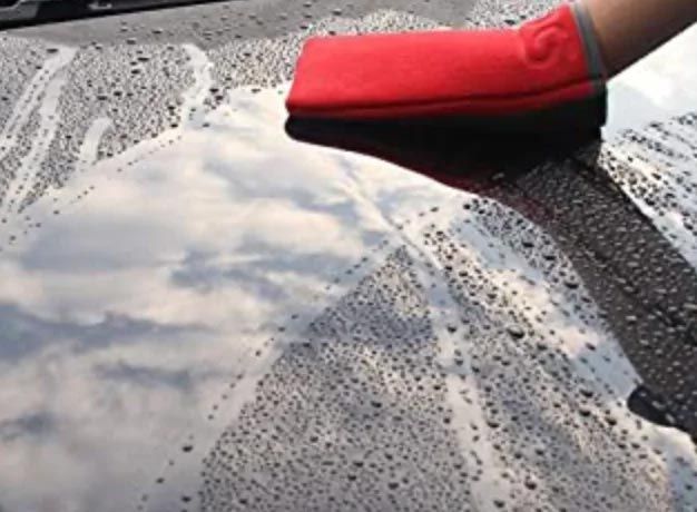 Red mitt wiping water and suds off a car windshield