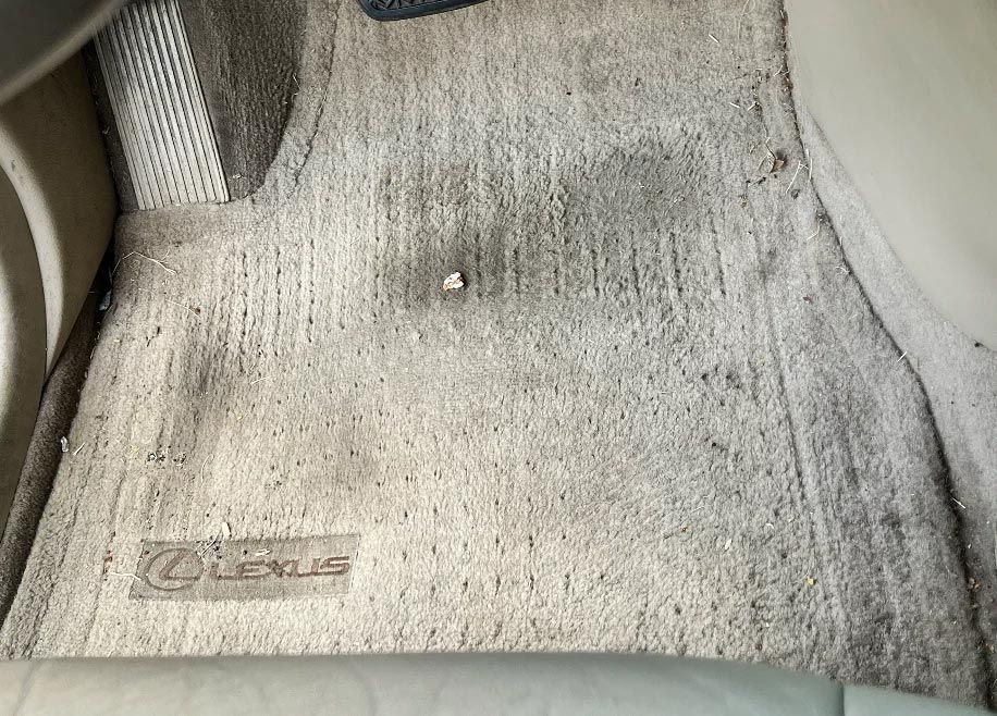 Dirty gray car floor mat with Lexus logo on the left side.
