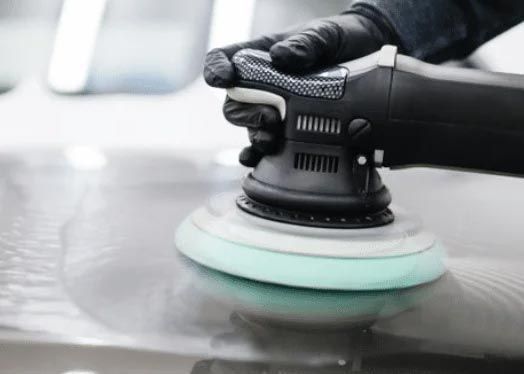 Gloved hand polishing a car hood with a buffer pad