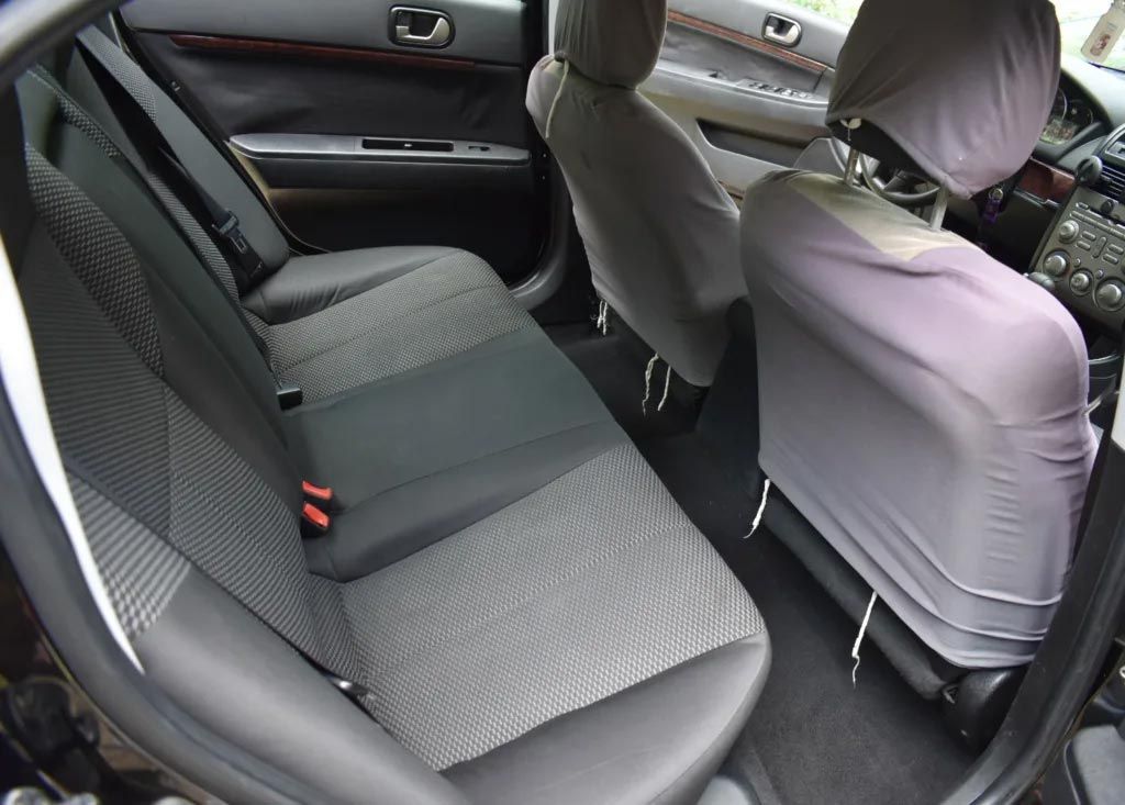 Car back seat with gray patterned upholstery and purple seat covers on the front seats.