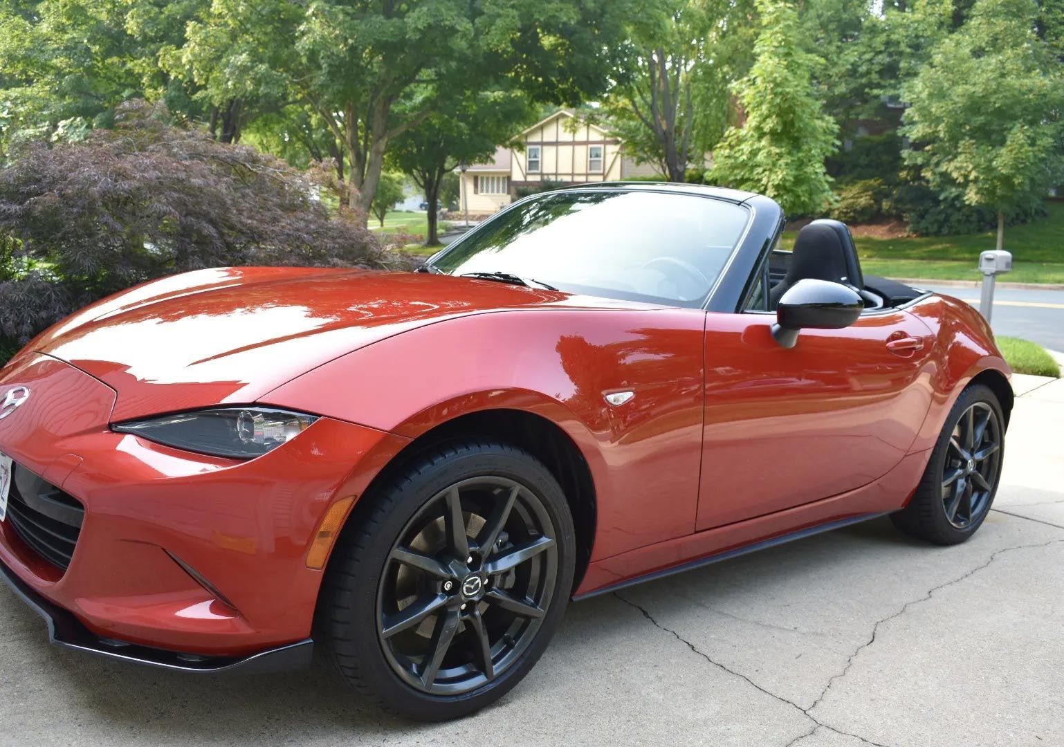 Red convertible sports car parked in a driveway with green trees in the background