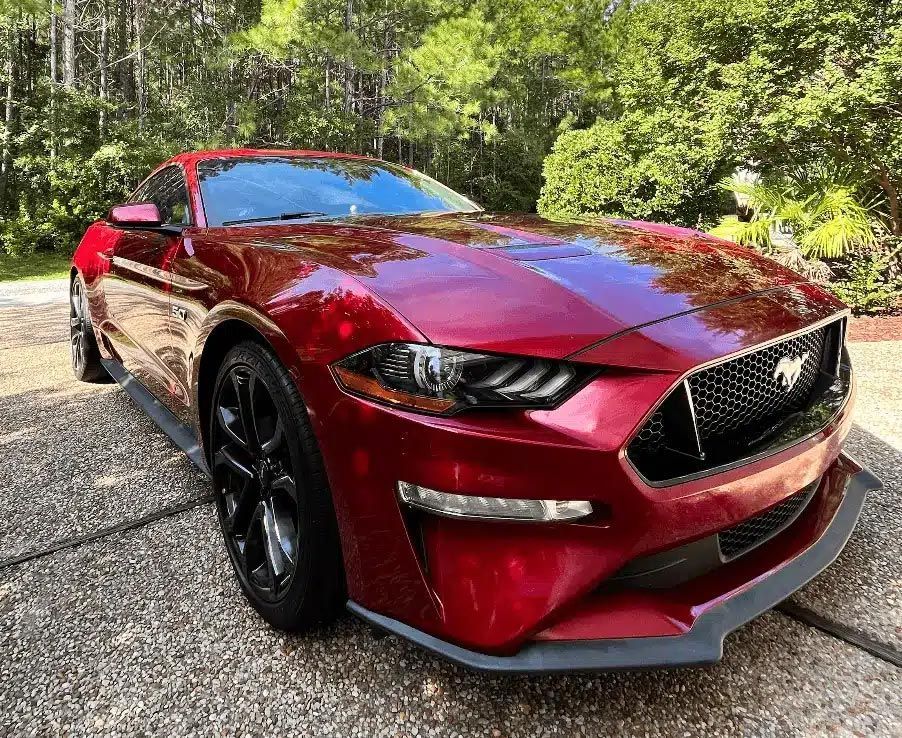 Red sports car parked on a wooded driveway, front three-quarter view with glossy paint.