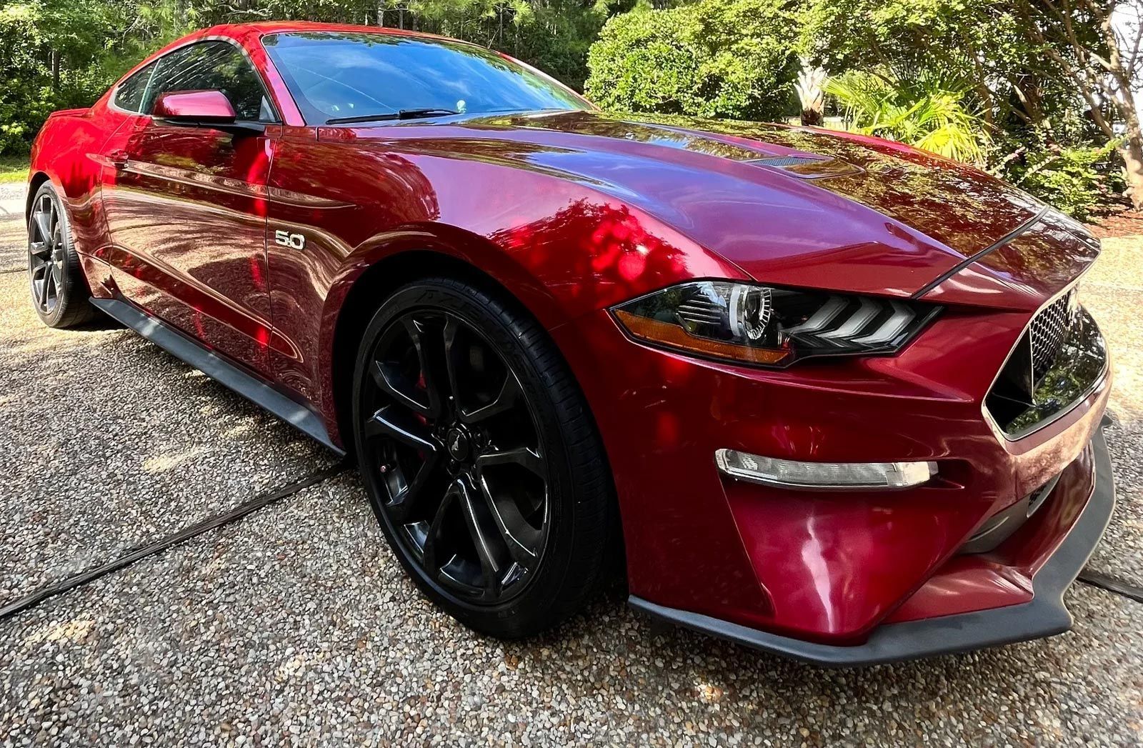 Red sports coupe parked on gravel, viewed from the front-left with black rims and a glossy finish