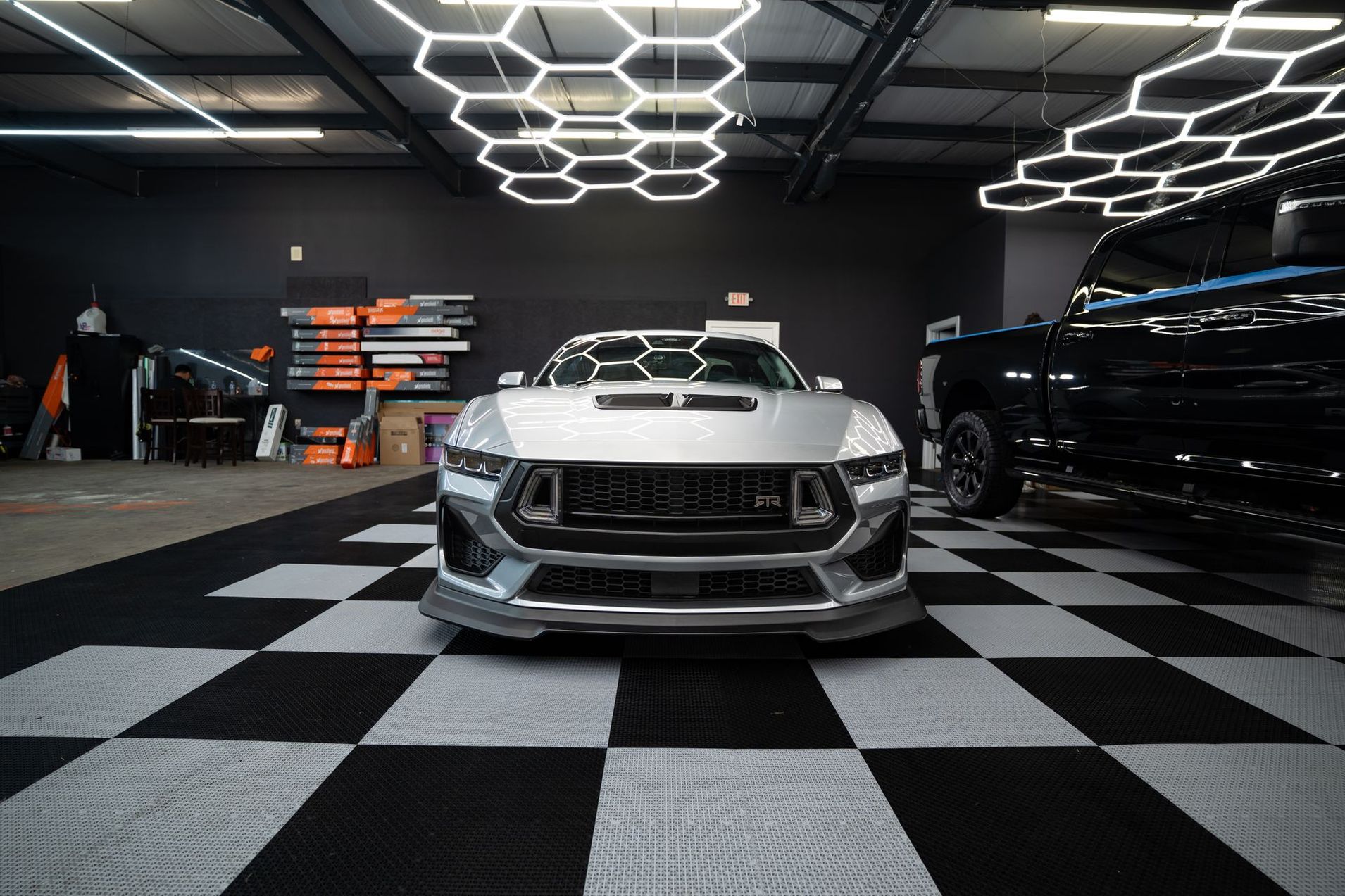 Silver sports car in a showroom with black-and-white checkered floor and hexagon ceiling lights