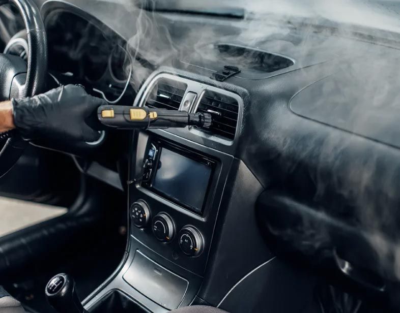 Car dashboard being disinfected with a spray gun, smoke or mist filling the interior.