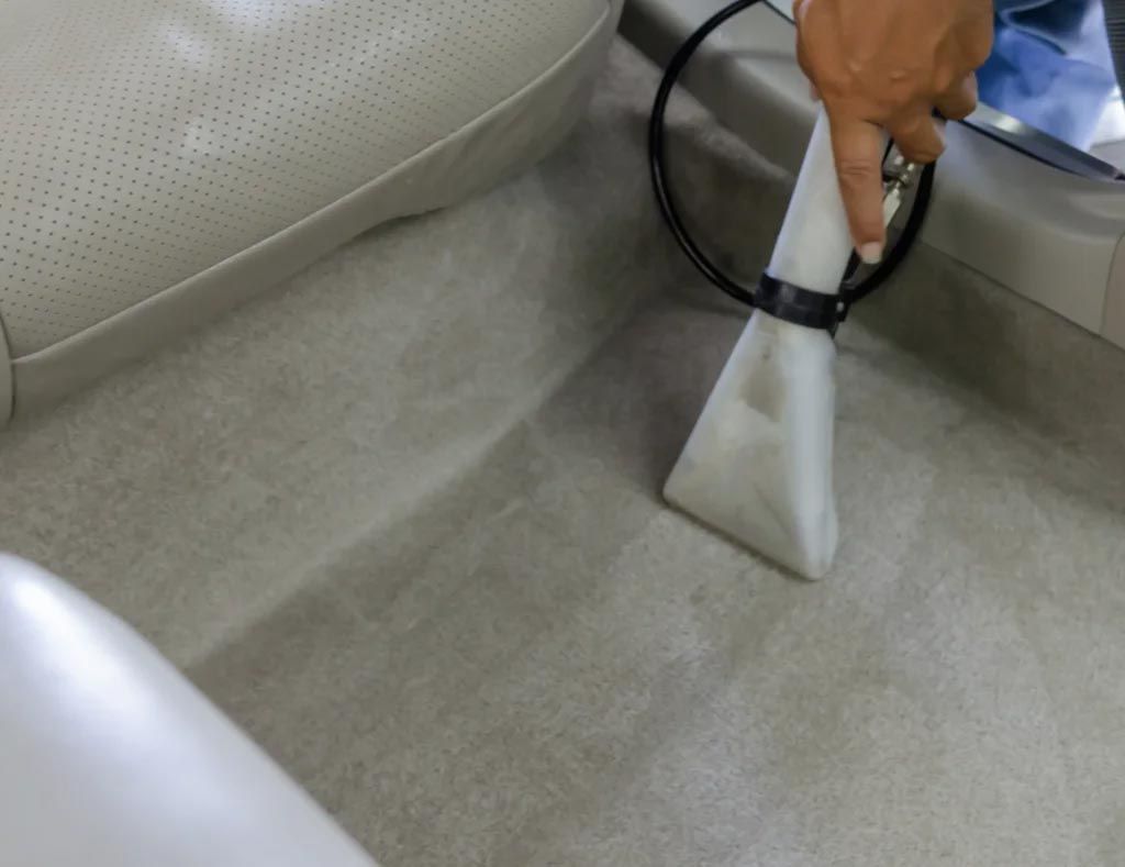 Person using a handheld carpet cleaner on a light gray carpet next to a couch