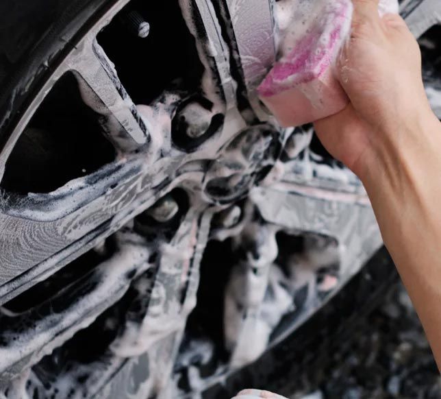 Person scrubbing a car wheel with pink foam and a sponge in a car wash