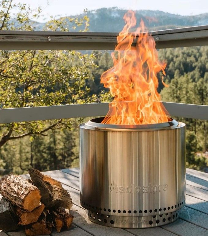 Stainless steel outdoor fire pit with visible flames on a wooden deck