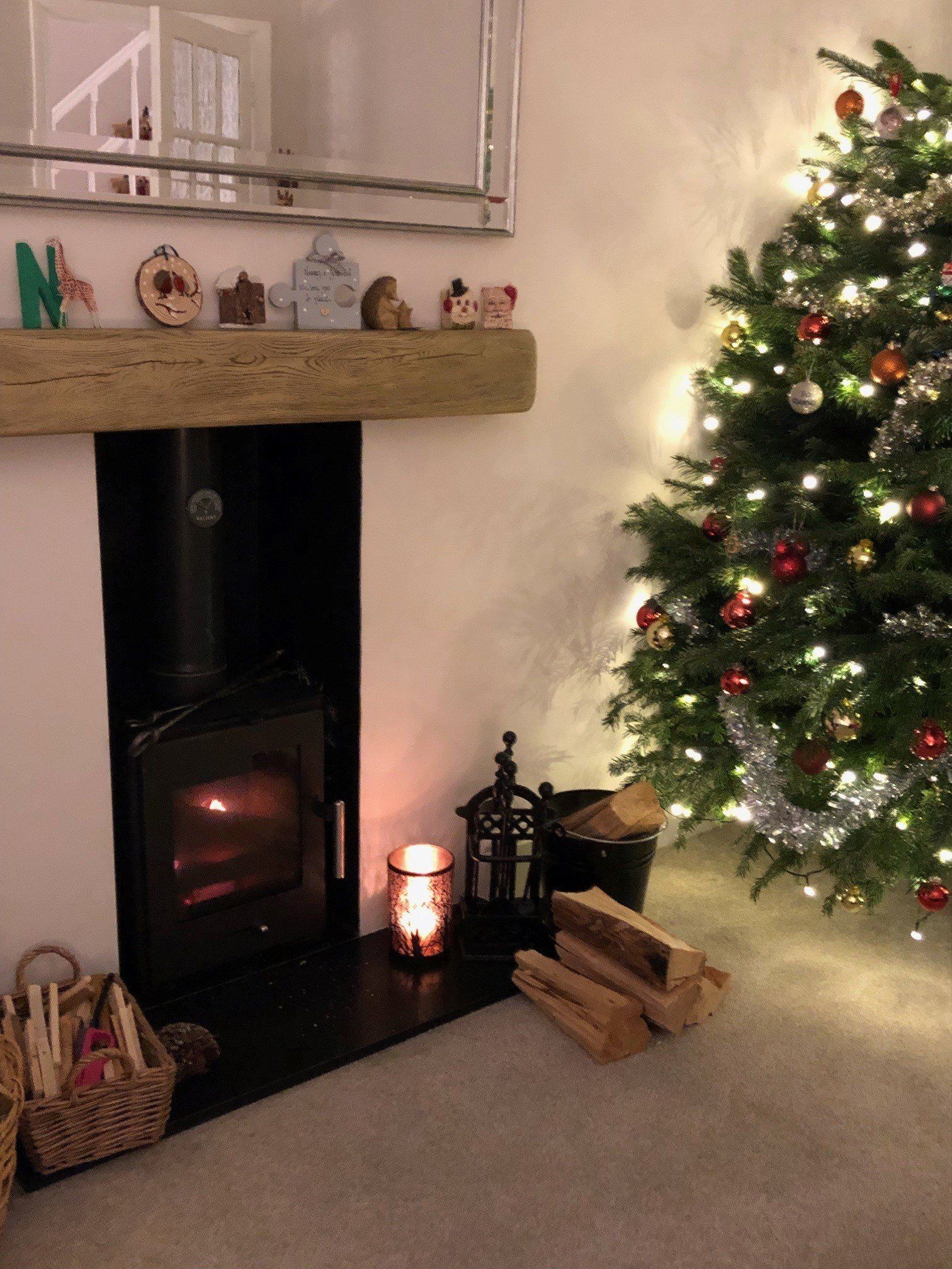 Wood burning stove with Christmas tree, festive lights, and cosy living room decor