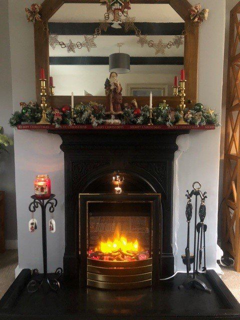 Decorative fireplace with festive mantel, candles, and glowing electric fire in a cosy living room