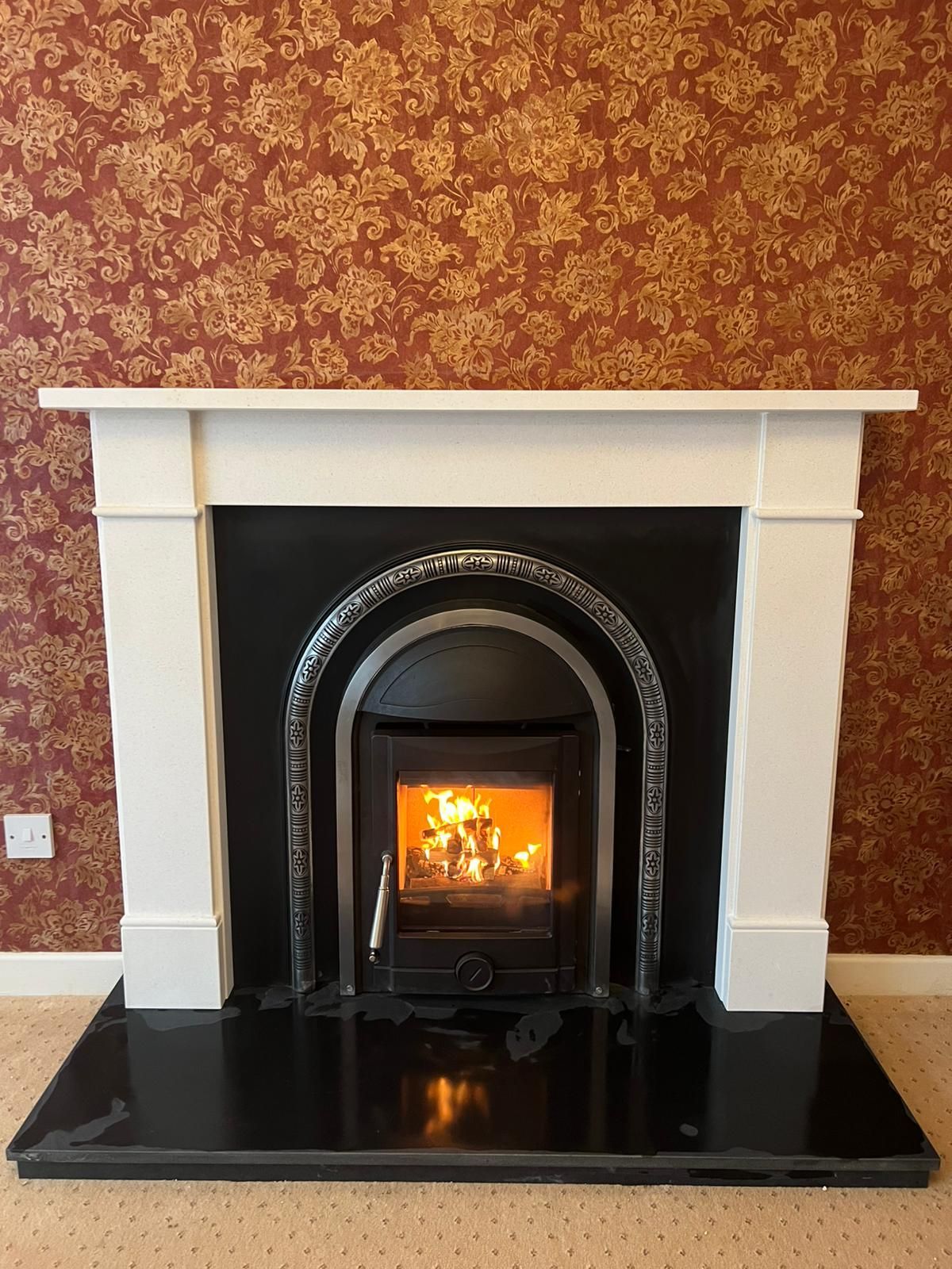 A stylish fireplace with a black stove and white surround, set against floral wallpaper