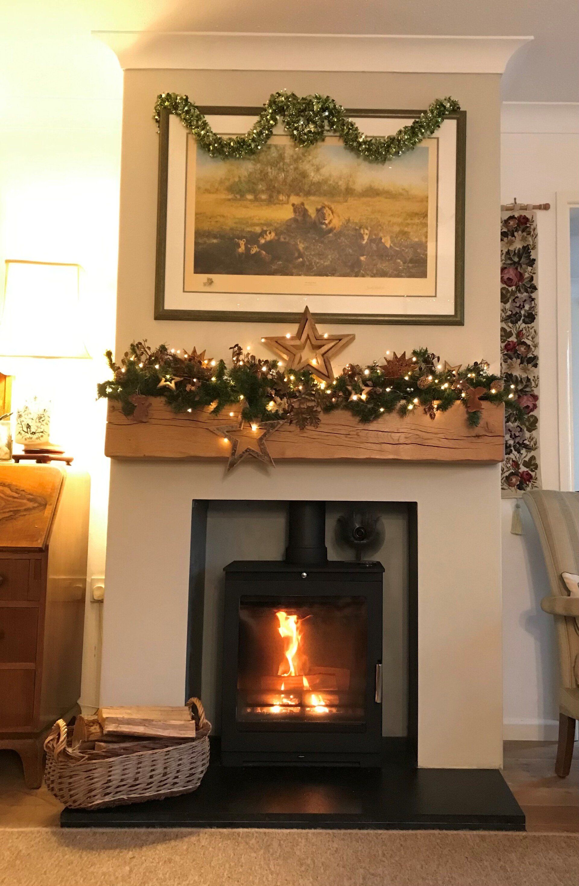 Wood burning stove with festive mantel decor, lights, and cosy living room setting