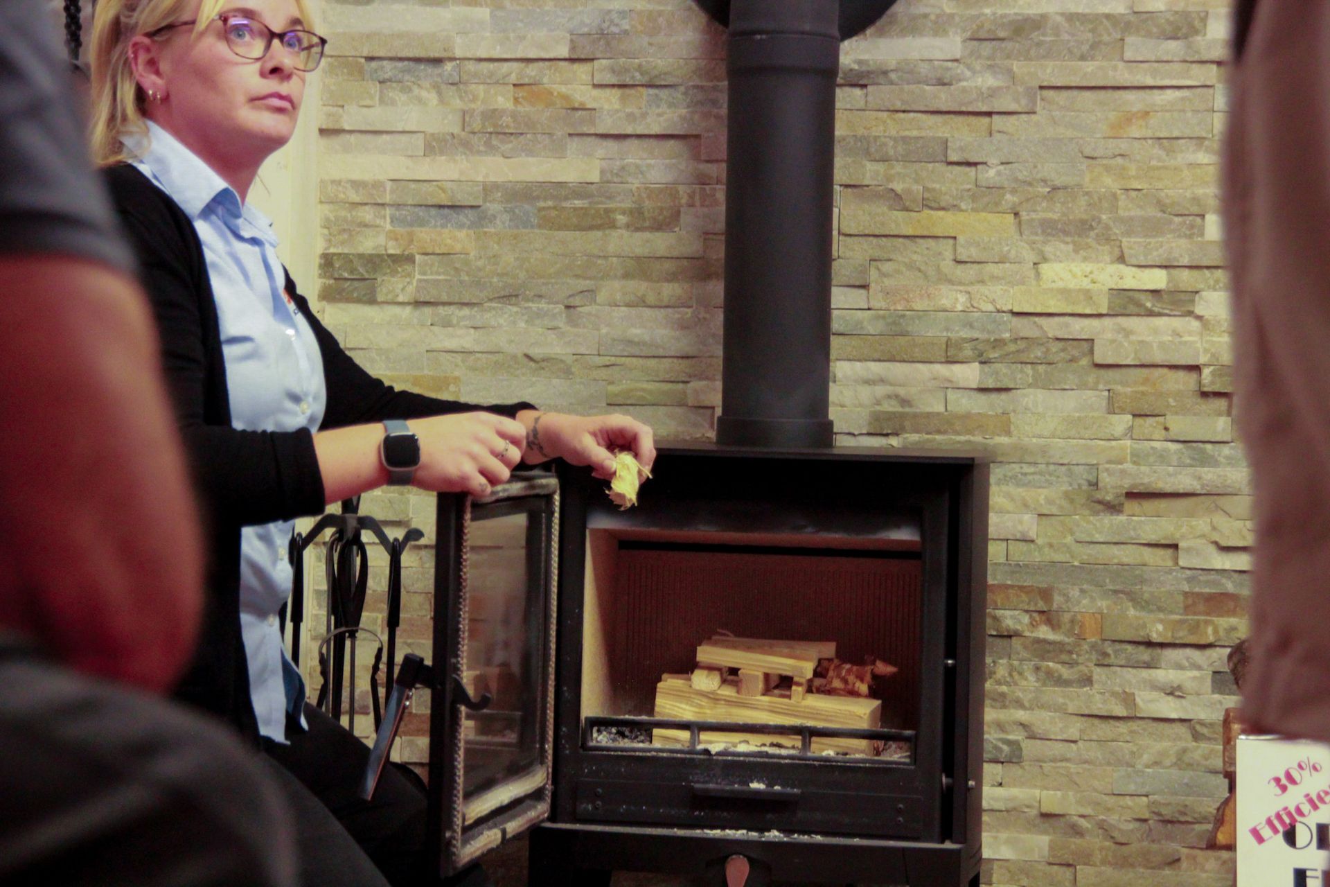 Person demonstrating how to use a wood-burning stove with logs inside