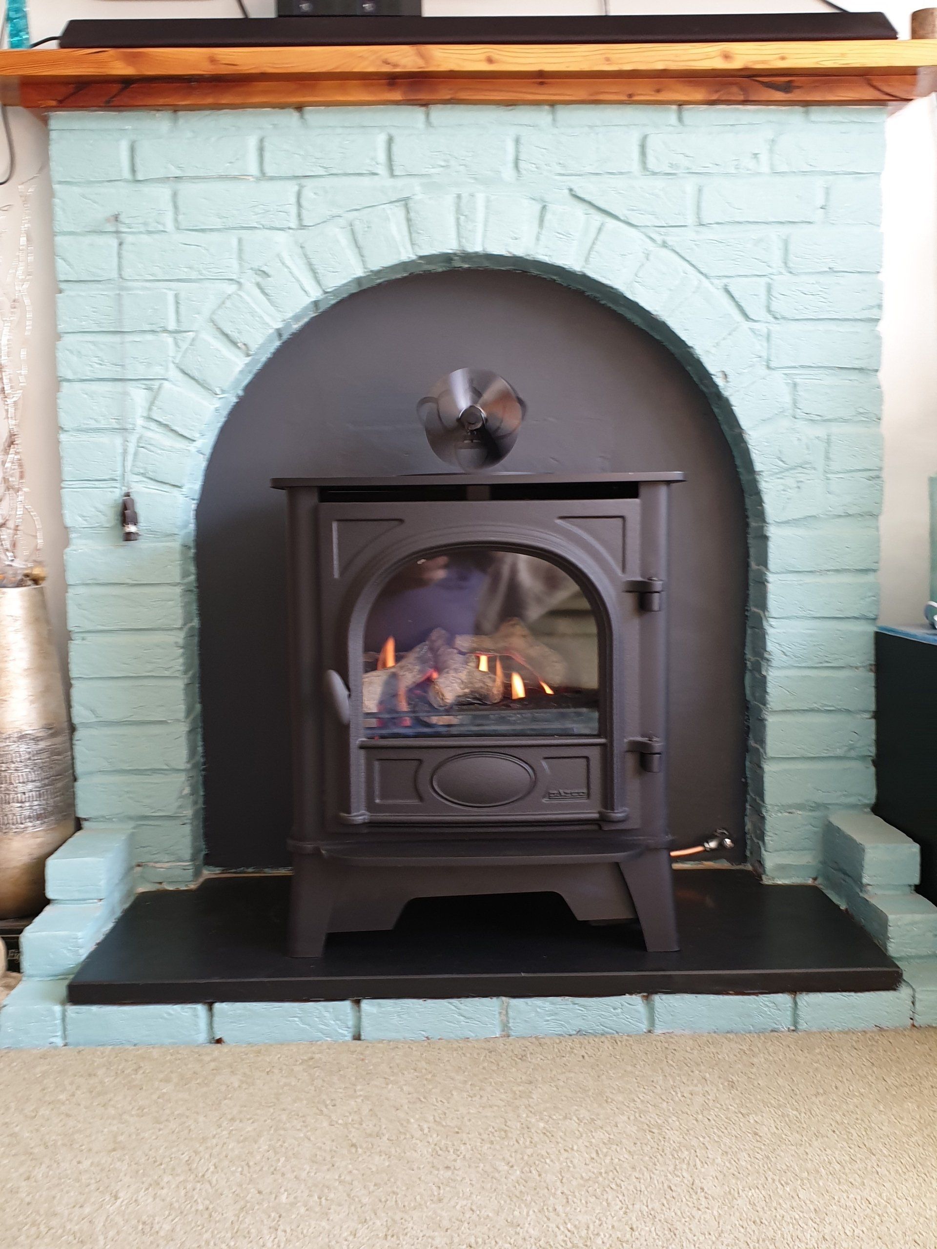 Wood burning stove in painted brick fireplace with arched opening and wooden mantel.