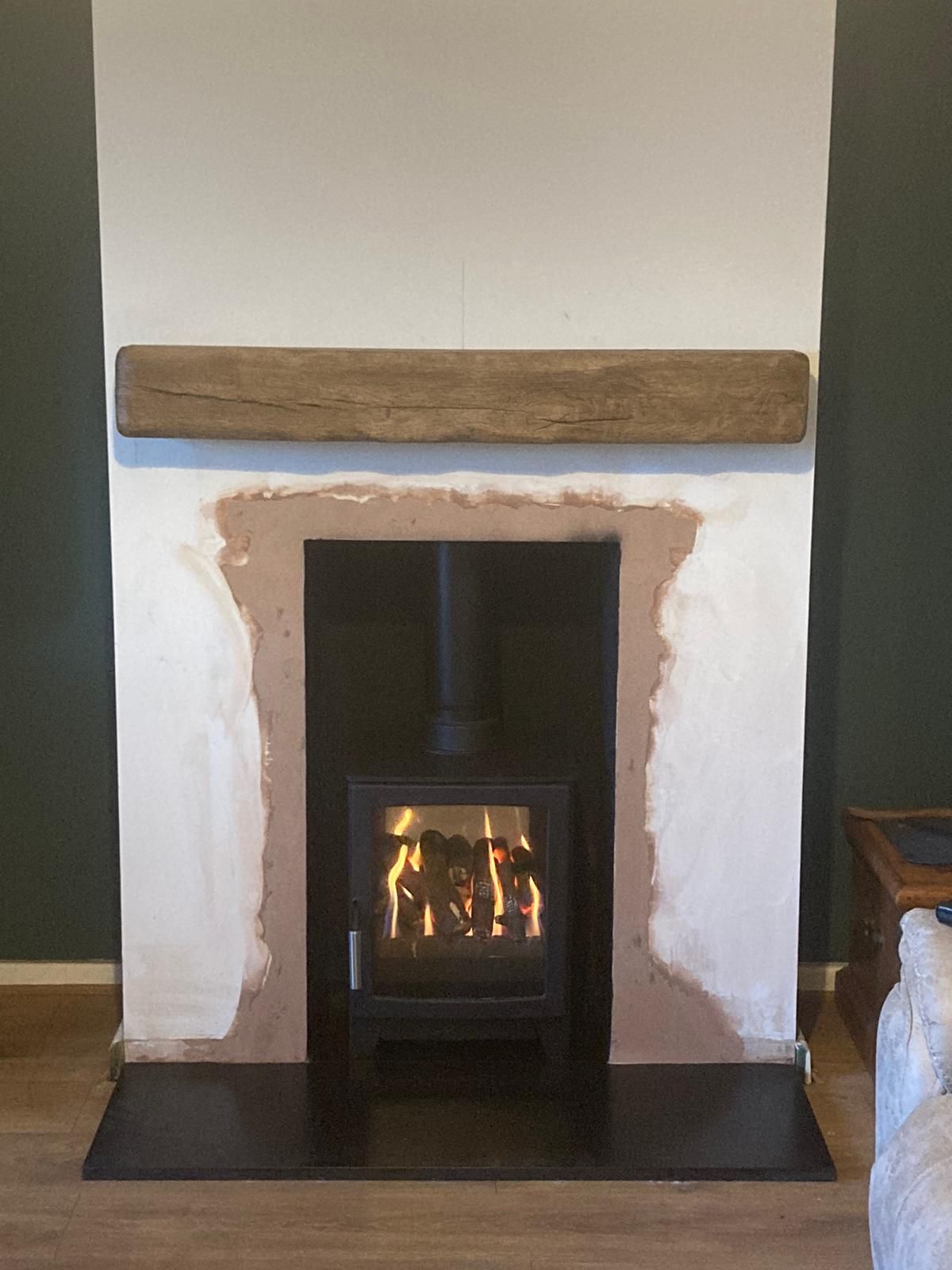 Wood burning stove with flame inside a simple plastered fireplace and wooden mantel