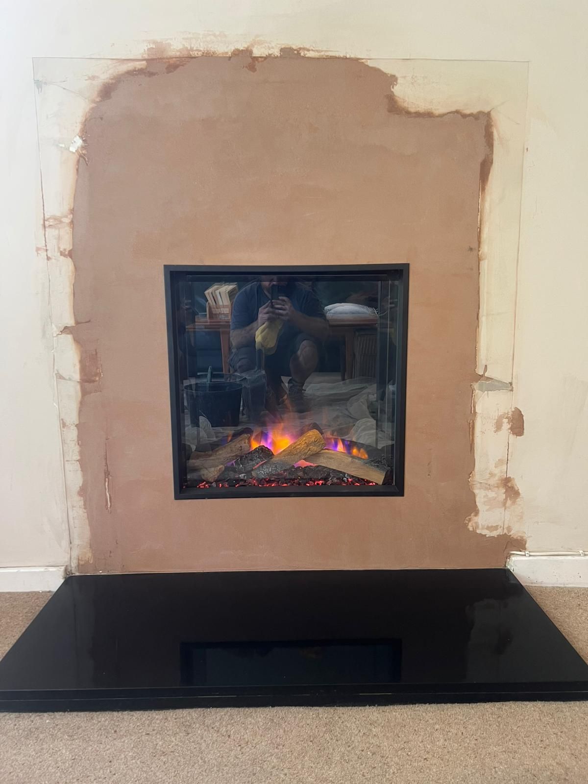 **In-progress installation of a modern fireplace with a sleek black base and framed glass front
