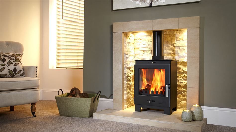 Cozy living room with a burning stove in a stone fireplace, armchair, and a basket of logs.
