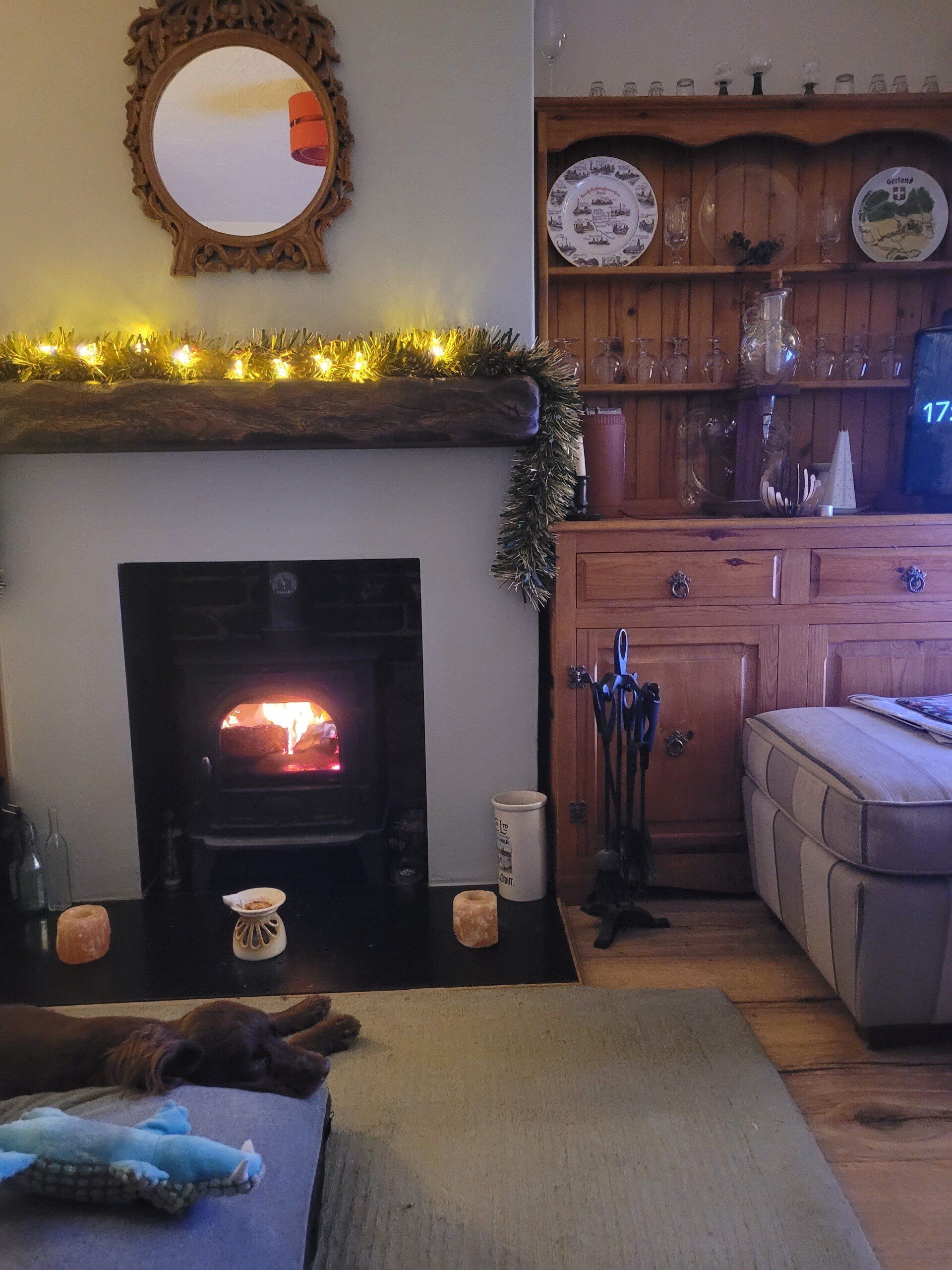 Wood burning stove with festive lights, rustic decor, and cosy living room with a resting dog