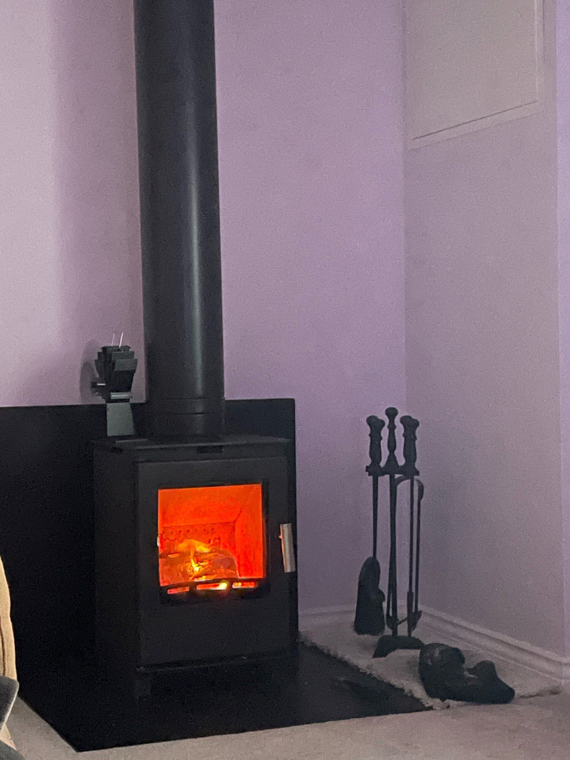 Black wood burning stove with glowing fire and fireplace tools in a minimalist corner setting