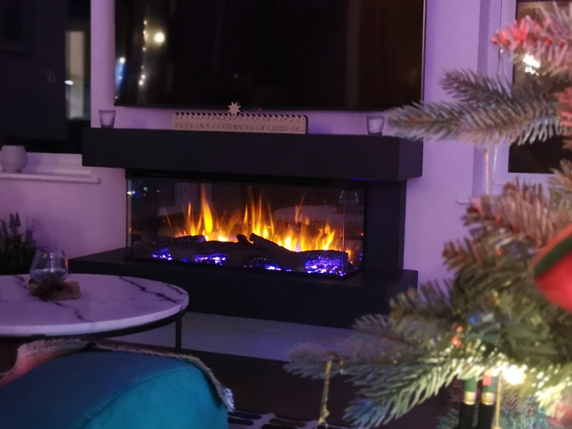 Modern electric fireplace with glowing flames in a cosy living room with festive decor and Christmas tree.