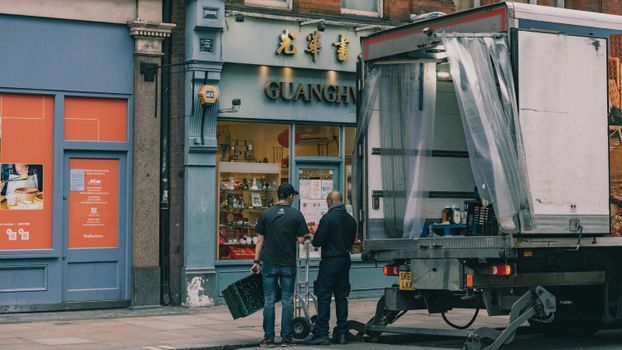 Dos personas conversando junto a un camión frente a una tienda azul con una puerta naranja.