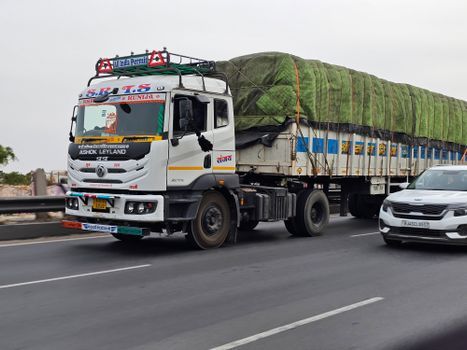 Camión de carga blanco con carga cubierta circulando por una autopista junto a un coche.