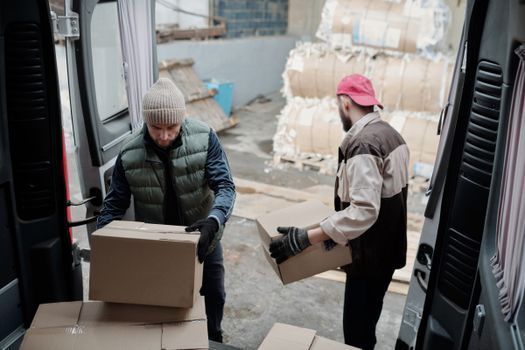 Dos trabajadores descargando cajas de cartón de una furgoneta en el patio de un almacén.