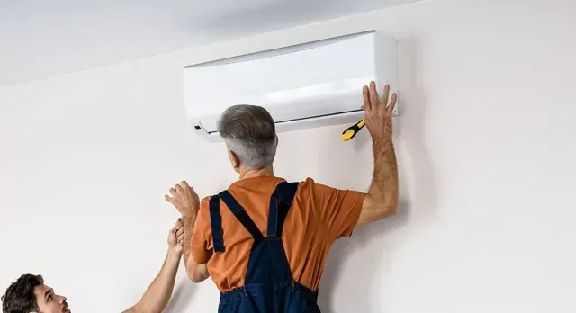 Deux hommes installent un climatiseur sur un mur.