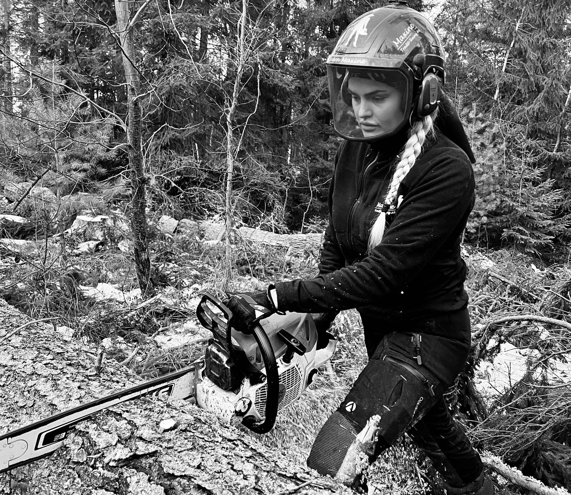 A woman wearing a helmet is using a chainsaw in the woods.