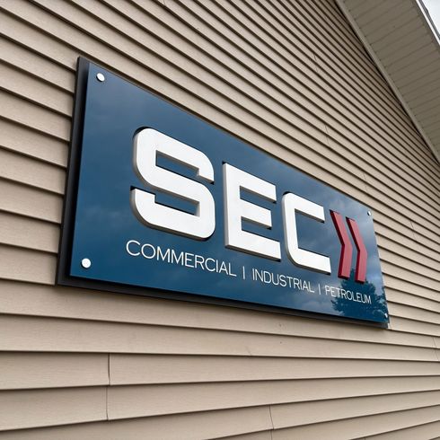 Sign for SEC, a commercial and industrial company, mounted on a tan building. White letters and logo on a blue background.