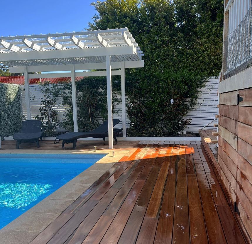 A Wooden Deck surrounded by swimming pool and white fence — Bloomscapes in Lennox Head NSW