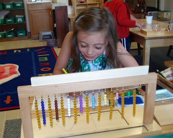 A person focused on using a Montessori bead frame learning tool in a classroom setting.
