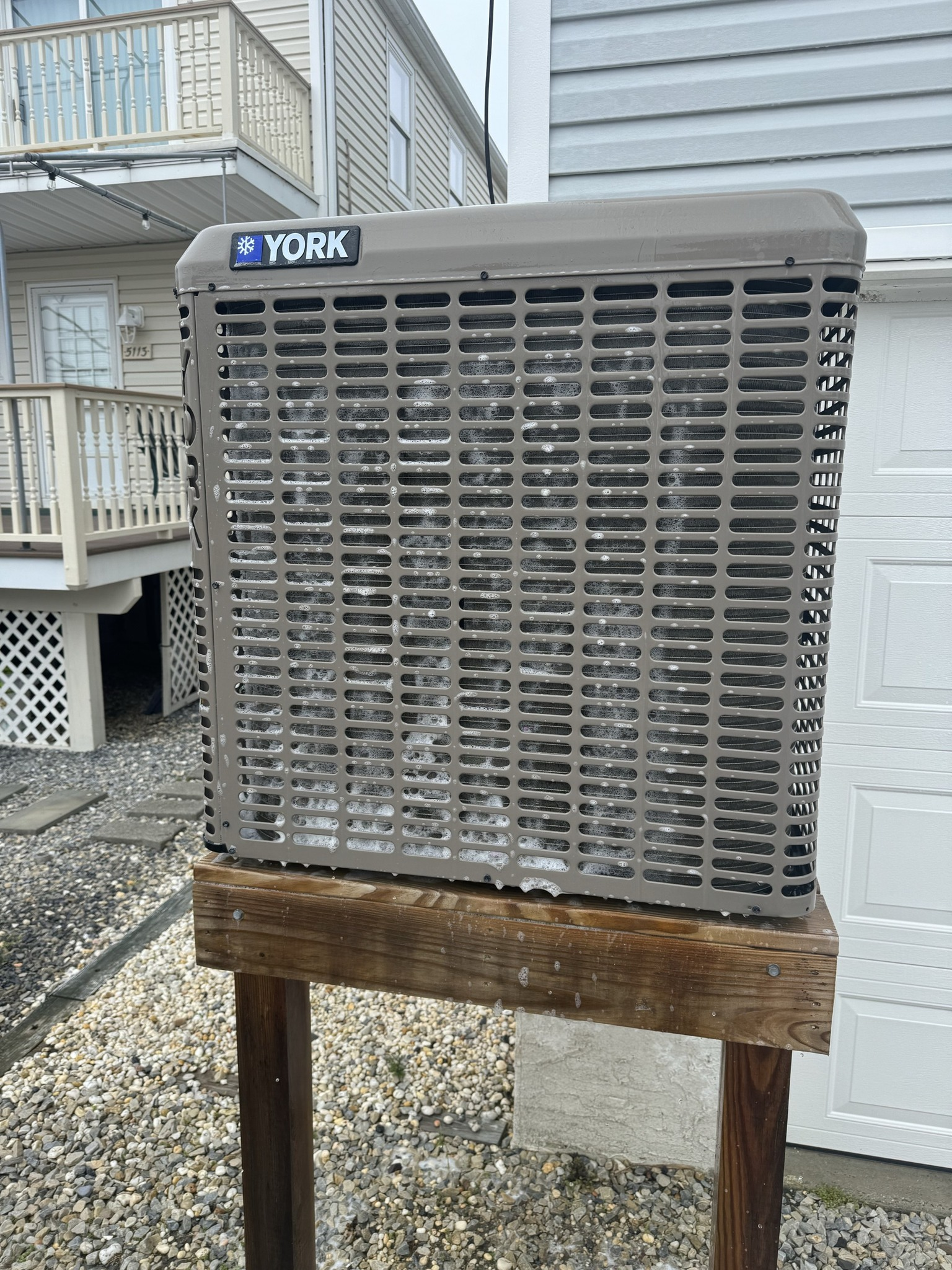 York air conditioning unit on a wooden stand. Gray and brown, outside a building.