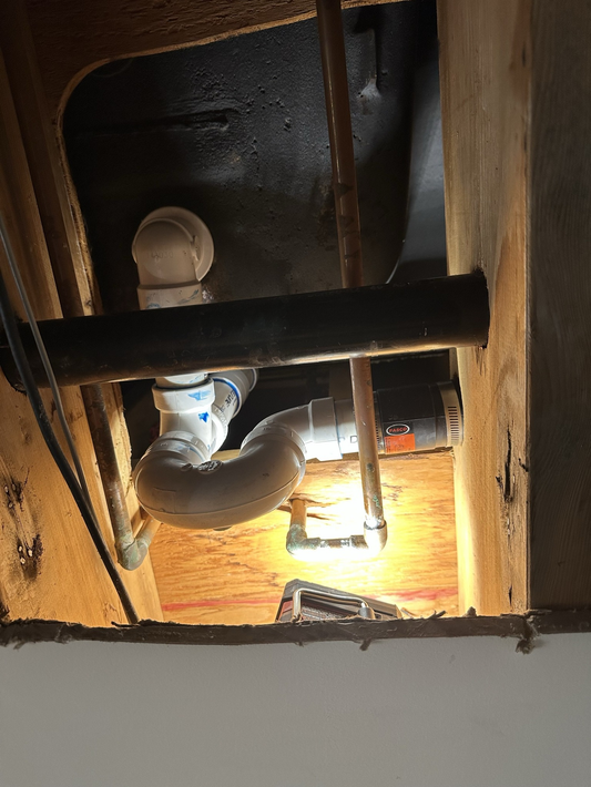 Plumbing pipes, including a white PVC P-trap, are installed inside a wood-framed ceiling cavity.