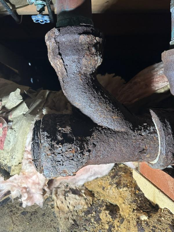 Corroded, old metal pipes in a dark, confined space. Rust and decay visible.