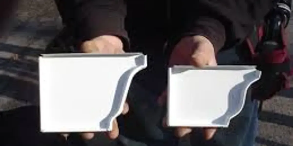 A person is holding two white gutters in their hands.