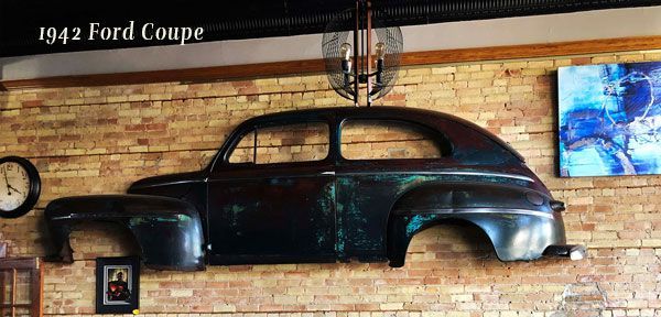 A 1942 ford coupe is hanging on a brick wall