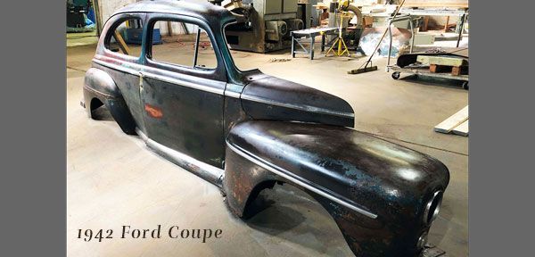 A 1942 ford coupe is being restored in a garage.