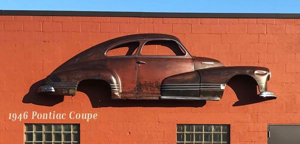 An old pontiac coupe is hanging on the side of a building